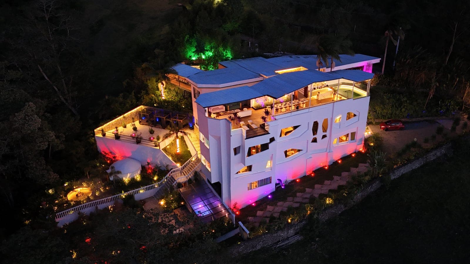 Casa de varios niveles iluminada al anochecer, vista desde un dron, tal como sale de cámara